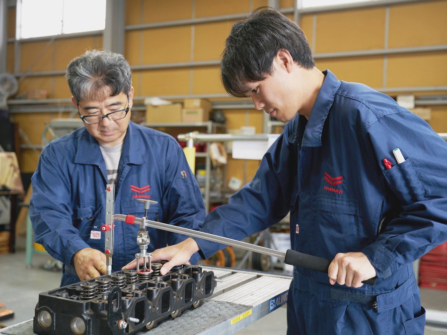 先輩社員と若手社員がエンジン部品を確認する様子